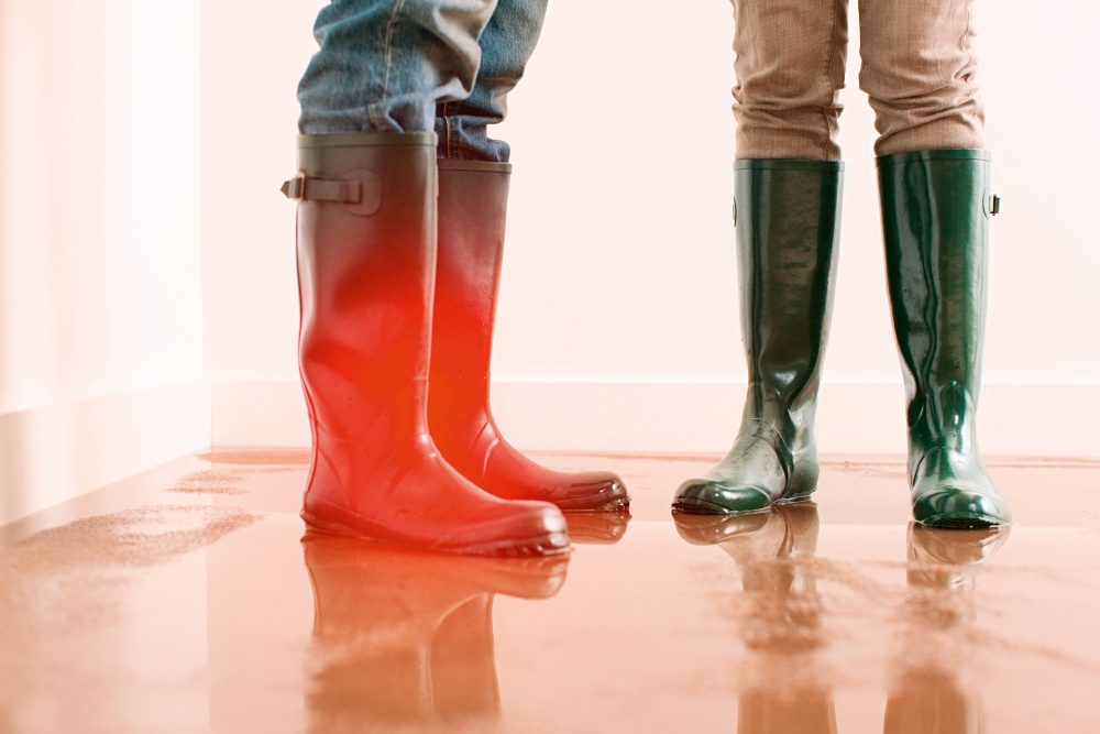 Ausschnitt zwei Personen mit Gummistiefeln auf nassem Boden im Haus