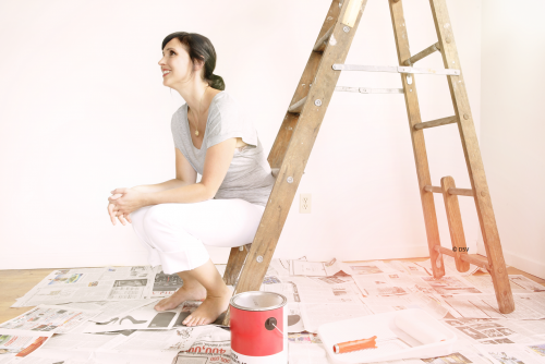 Frau sitzt auf einer Leiter in einer frisch gestrichenen Wohnung