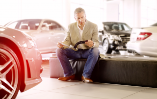 Mann sitzt im Autohaus und blättert durch die Autozeitschrift