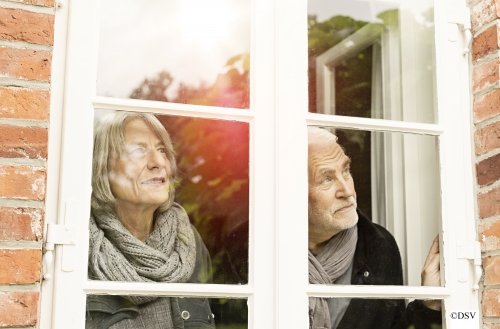 ältere Dame und älterer Herr schauen durch ein Fenster