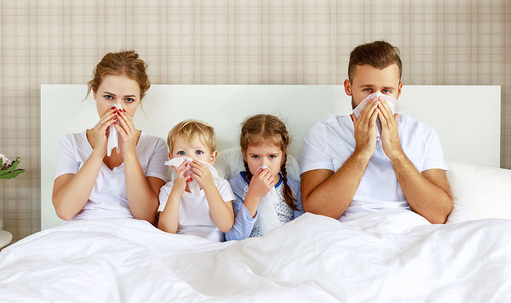 Familie mit Kindern krank im Bett mit Taschentüchern
