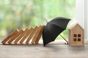Sinnbild: Regenschirm schützt Haus vor Gefahren - Wichtige Versicherungen bei der Baufinanzierung