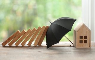 Sinnbild: Regenschirm schützt Haus vor Gefahren - Wichtige Versicherungen bei der Baufinanzierung