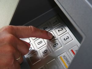 Jemand gibt seine PIN Nummer auf der Tastatur des Geldautomaten ein