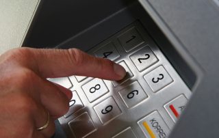Jemand gibt seine PIN Nummer auf der Tastatur des Geldautomaten ein