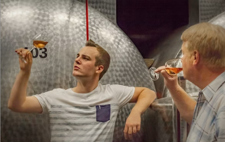 Zwei Männer verkosten Wein vor großen Edelstahltanks