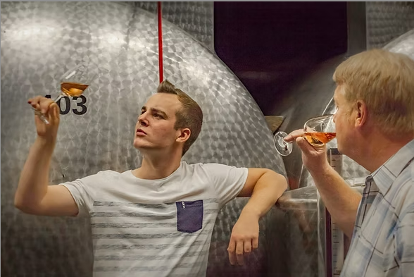 Zwei Männer verkosten Wein vor großen Edelstahltanks