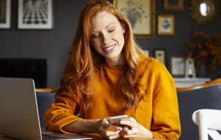 Ein Frau blickt lächelnd auf Ihr Smartphone.